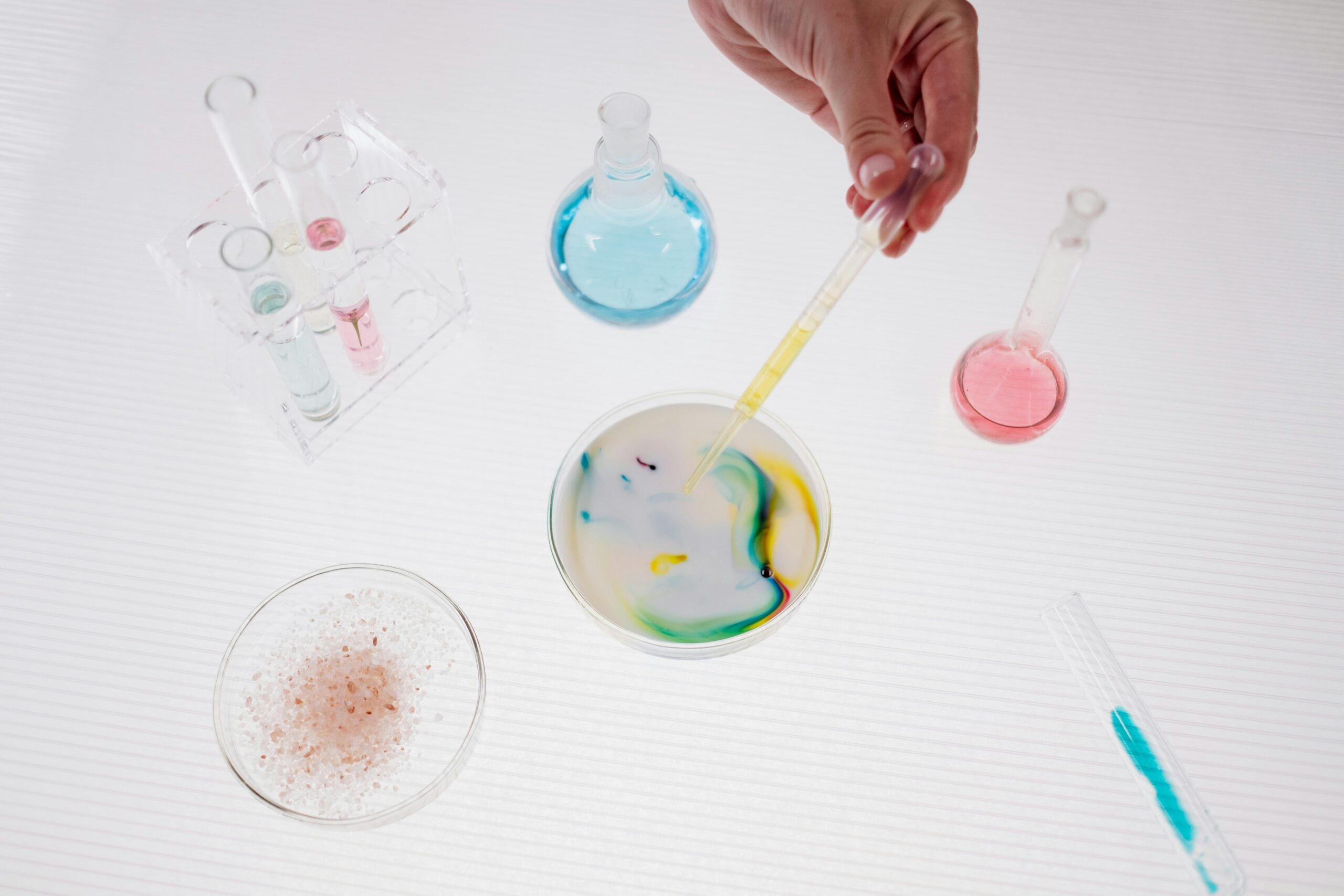 A top-down view of a colorful lab experiment with a hand holding a pipette over a petri dish.