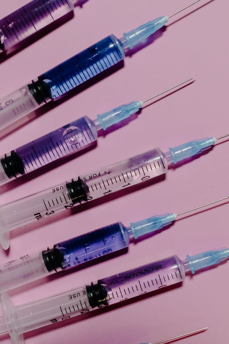 Several syringes with blue liquid on a pink background, showcasing medical equipment.